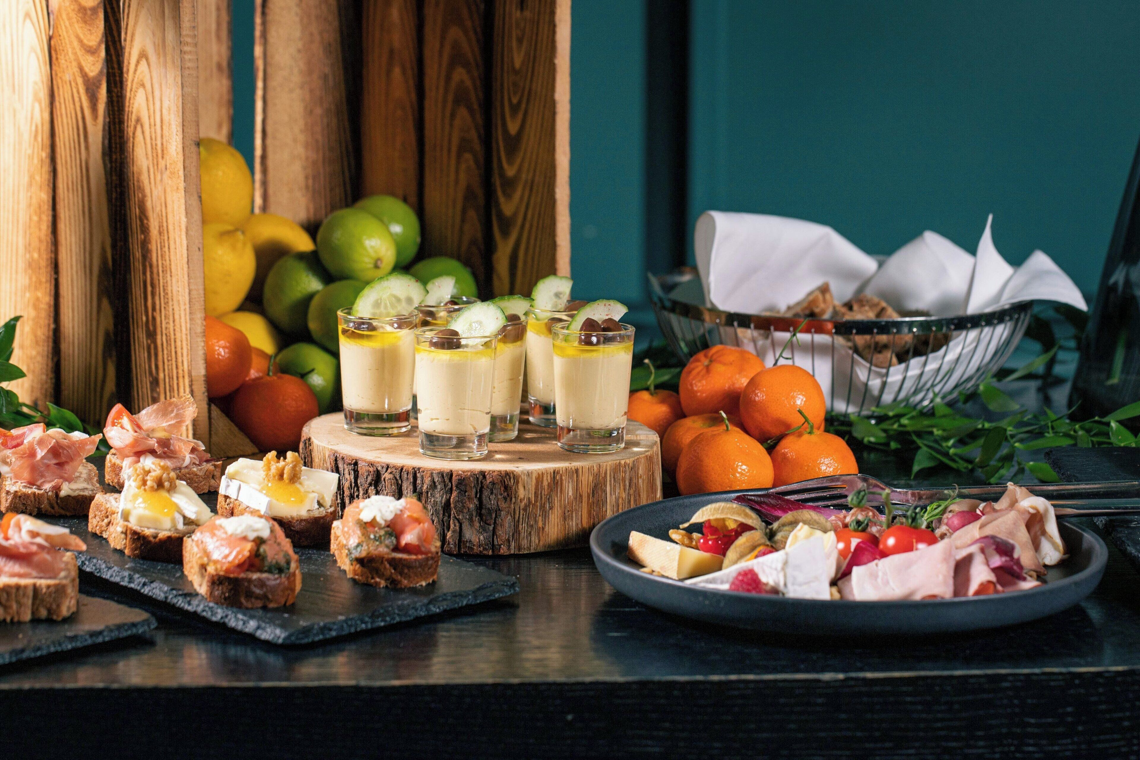 A variety of food items including sandwiches, fruits, and a plate of meat arranged on a wooden table.