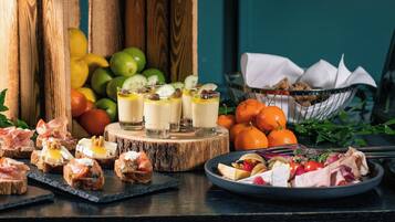 Diversos alimentos, incluindo sanduíches, frutas e um prato de carne, dispostos sobre uma mesa de madeira.