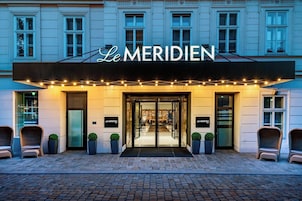 Exterior del hotel Le Meridien, con fachada clásica, puertas de entrada y plantas en macetas.