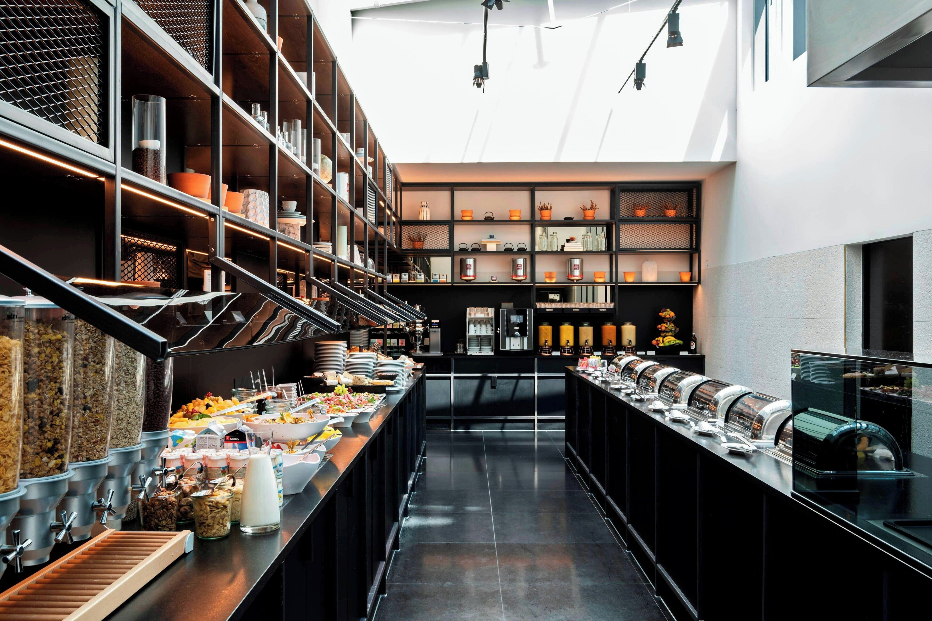 A modern kitchen with a long counter, various food dispensers, and shelves with kitchenware.