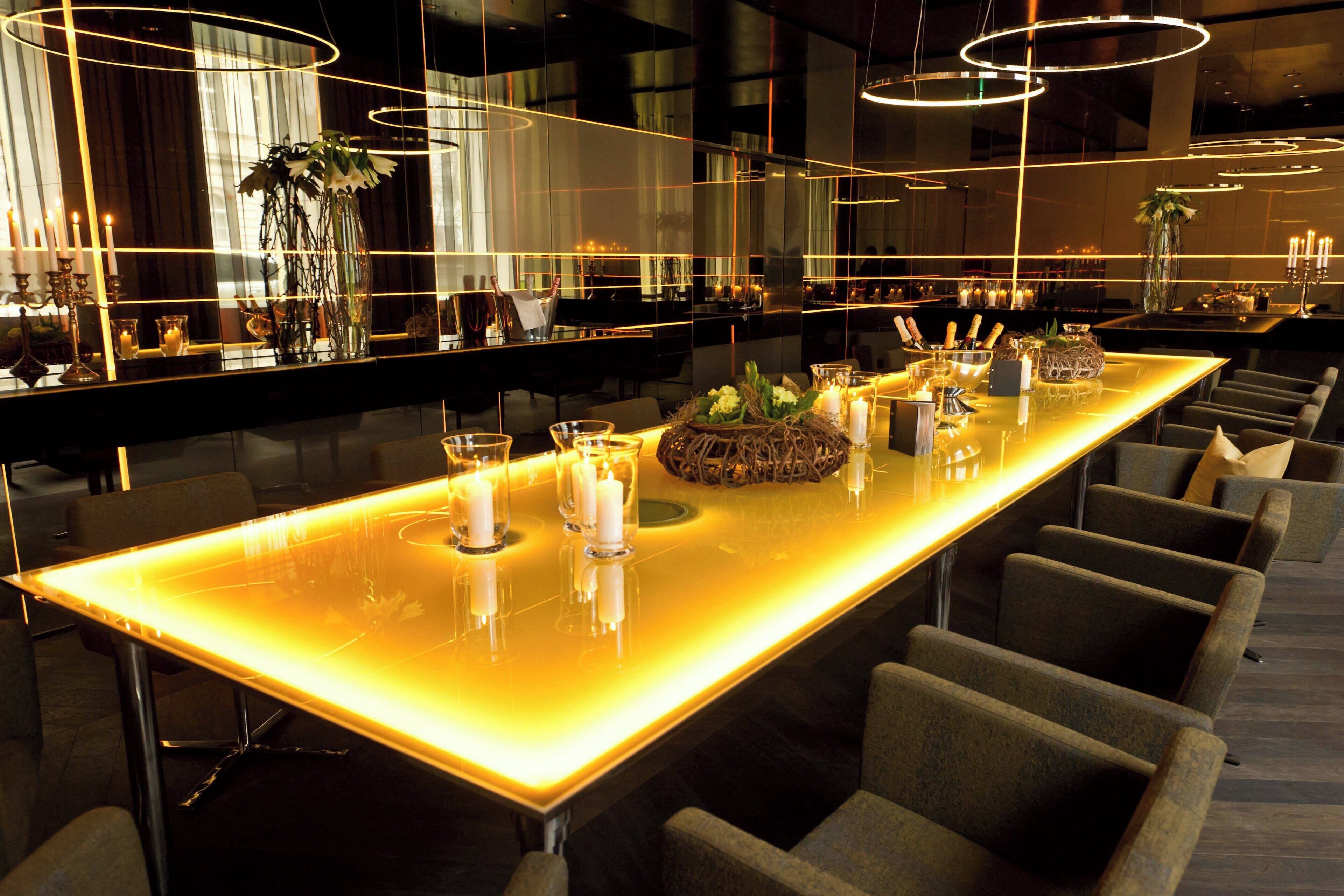 Un'ampia zona bar illuminata con una superficie riflettente, numerose candele e un elemento decorativo centrale.