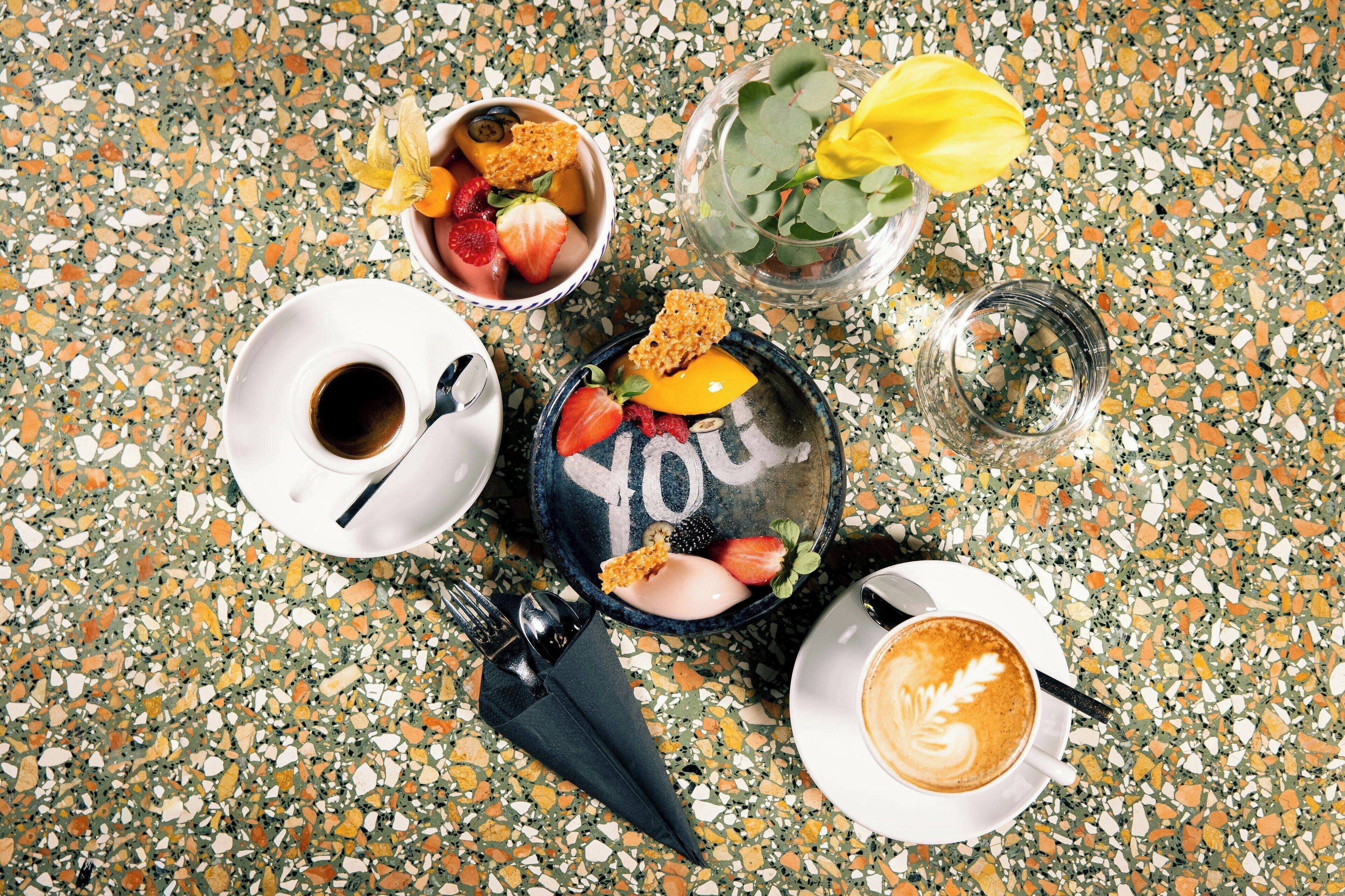 Une table avec une tasse de café, un bol de fruits, un verre d’eau et une assiette sur laquelle est écrit le mot « VOUS ».