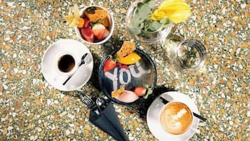 Uma mesa com uma xícara de café, uma tigela de frutas, um copo de água e um prato com a palavra 'YOU'.