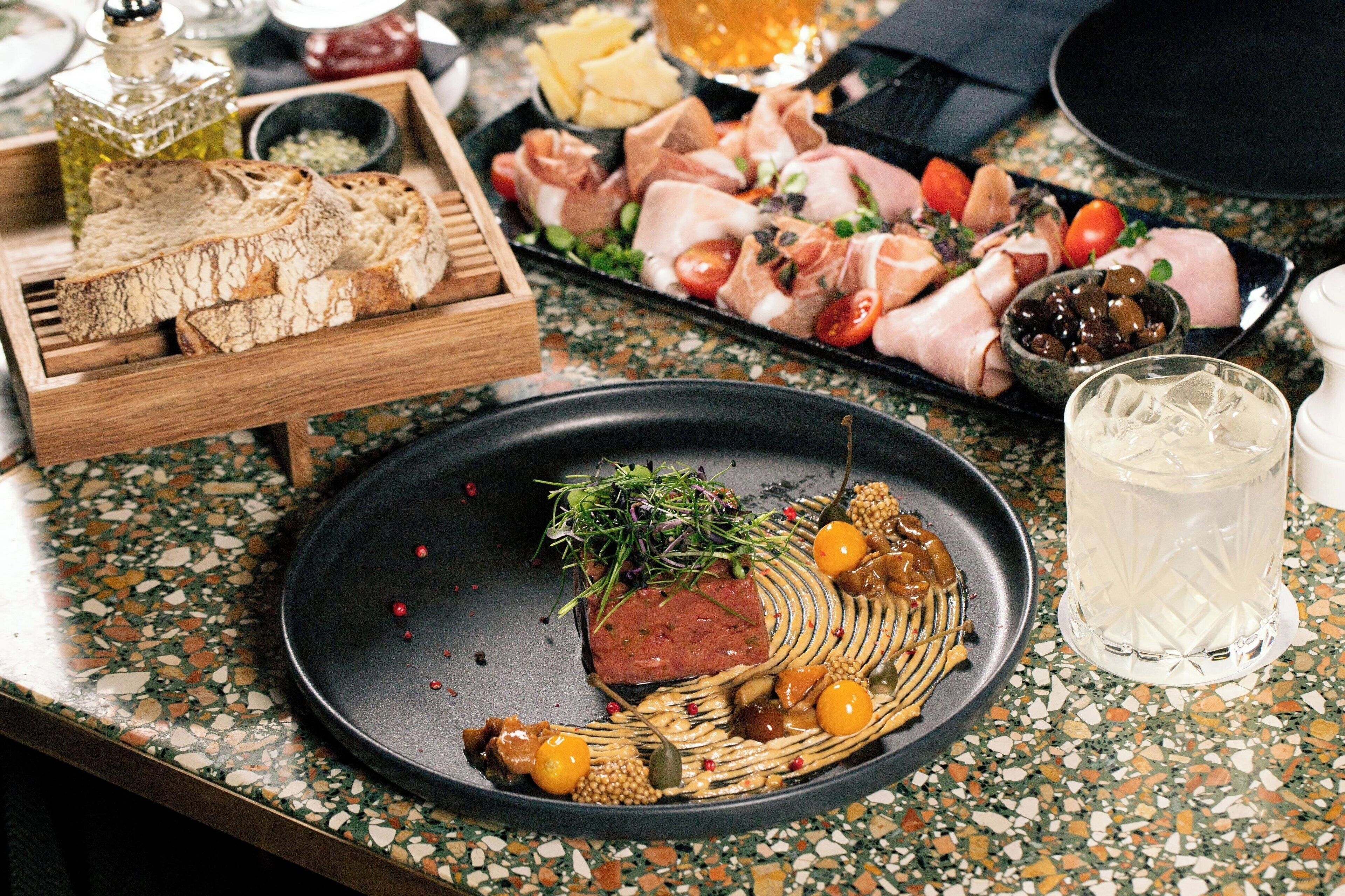 Een eettafel met diverse etenswaren, waaronder brood, vlees en groenten, en een glas water.