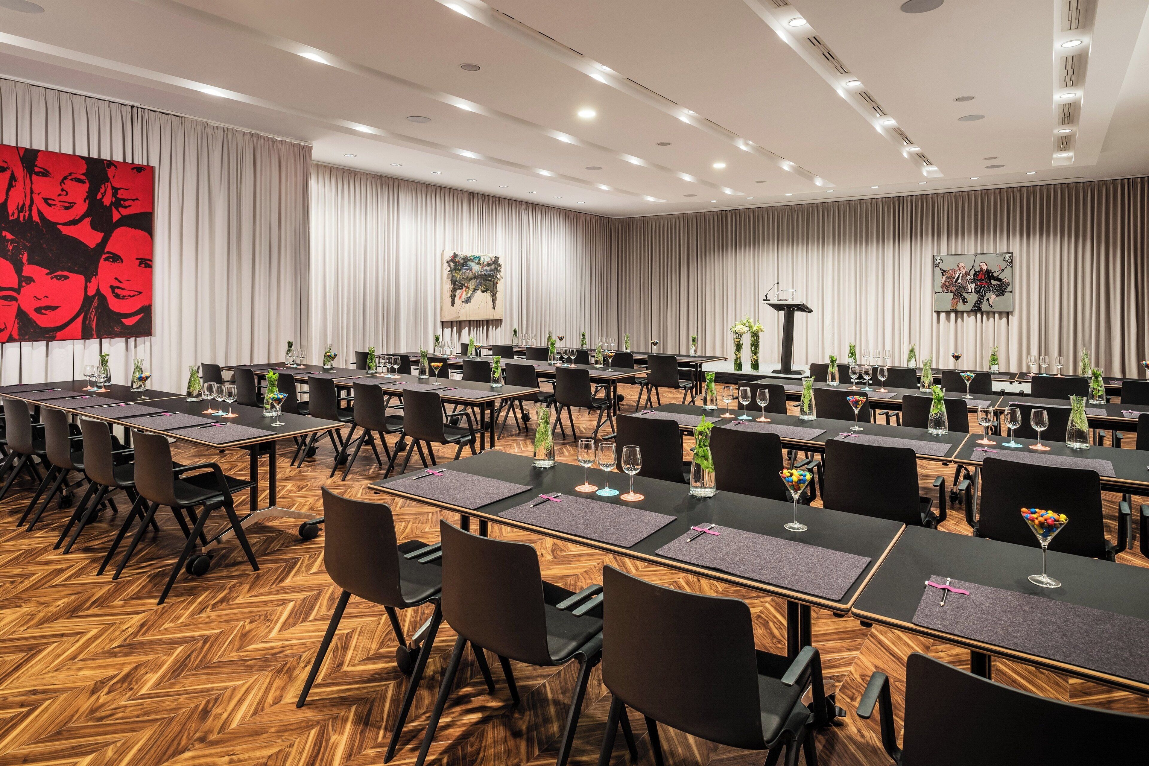 A conference room with multiple tables, black chairs, and a wooden herringbone floor.
