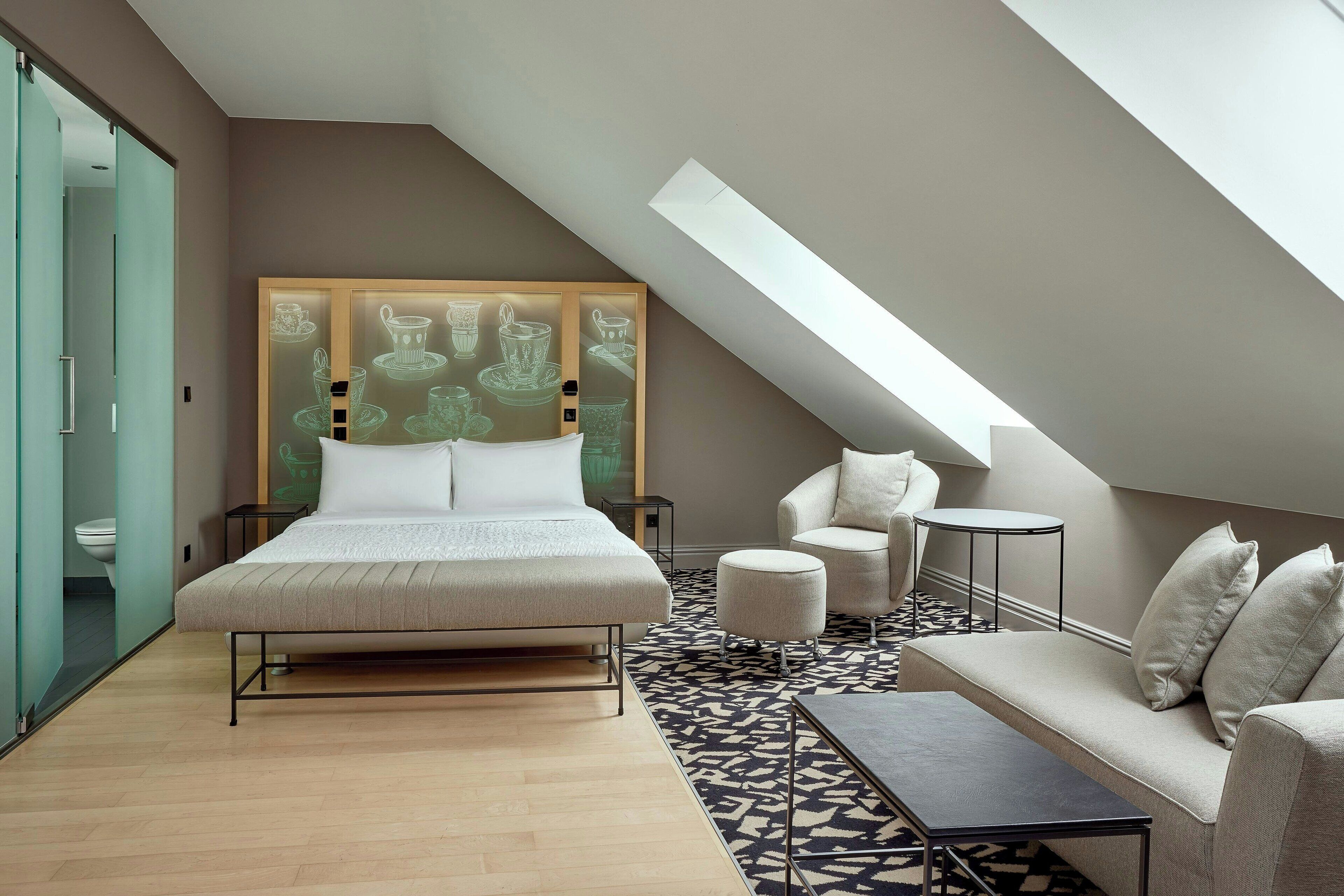 Un dormitorio moderno con una cama grande, un sofá, una mesita pequeña y una obra de arte original en la pared.