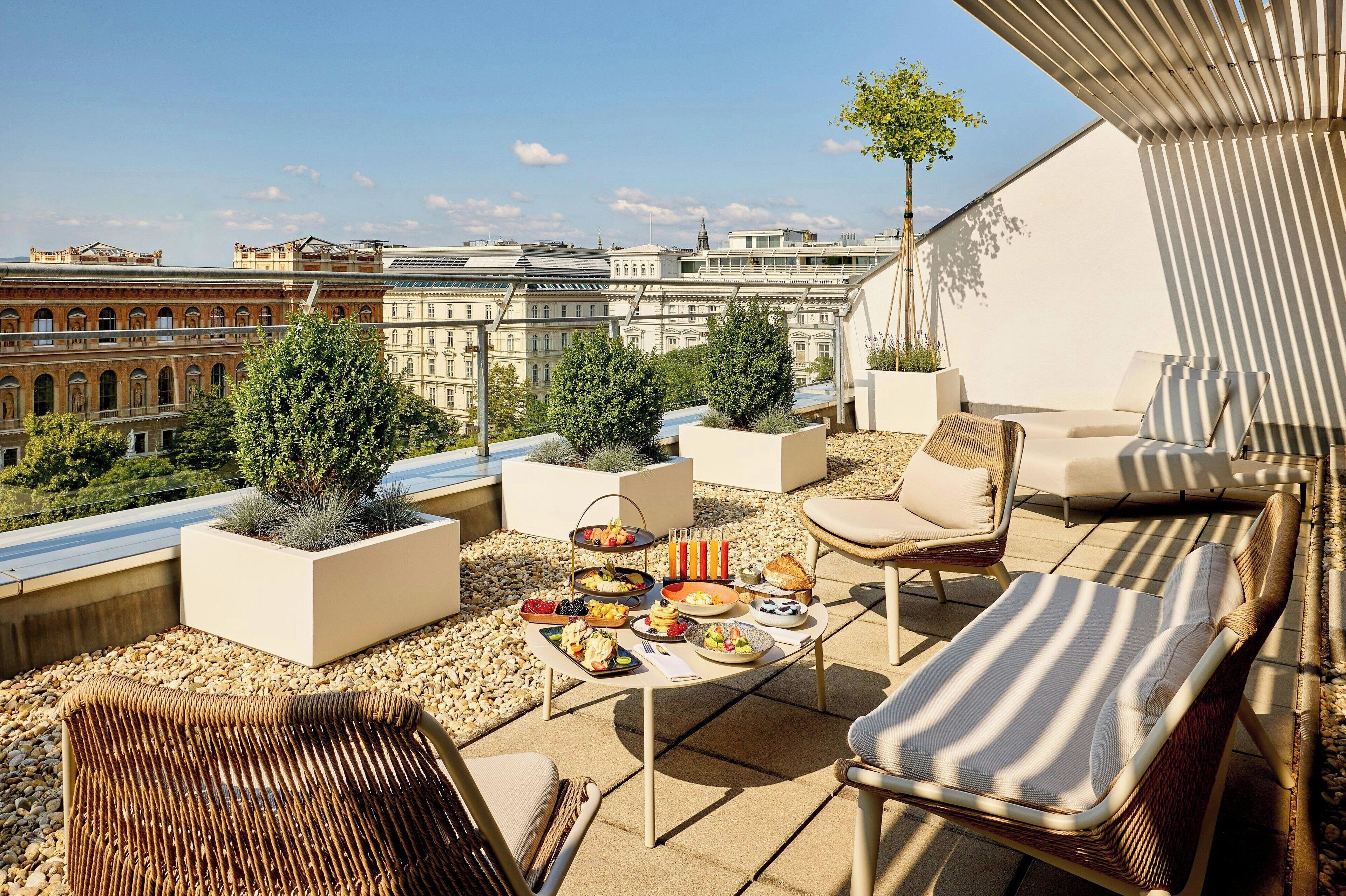 A rooftop terrace with outdoor seating, a dining table with food, and a cityscape view.