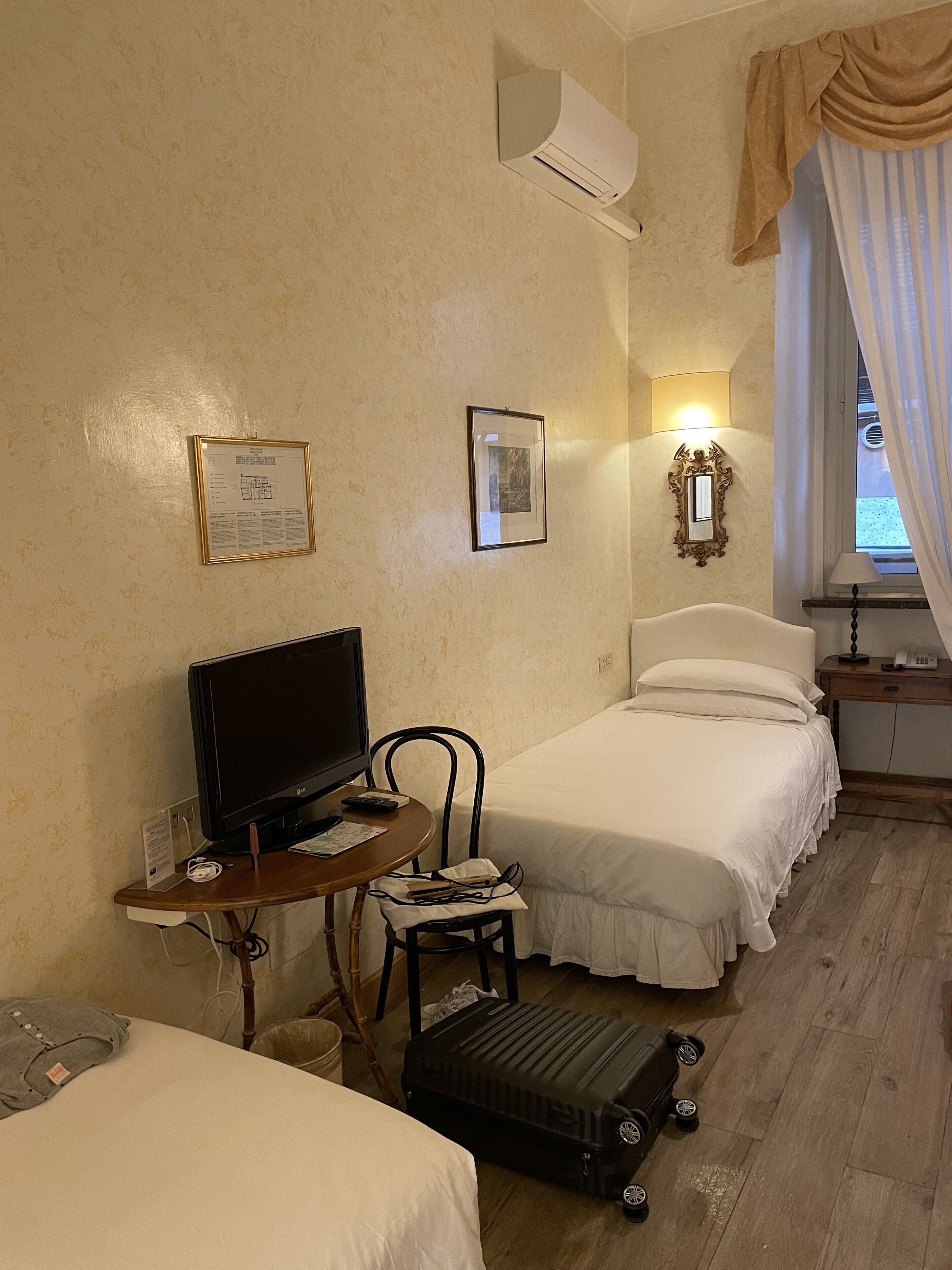 A hotel room with two beds, a television, a desk with a chair, and a suitcase on the floor.
