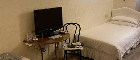 A hotel room with two beds, a desk with a computer, a chair, and a suitcase.