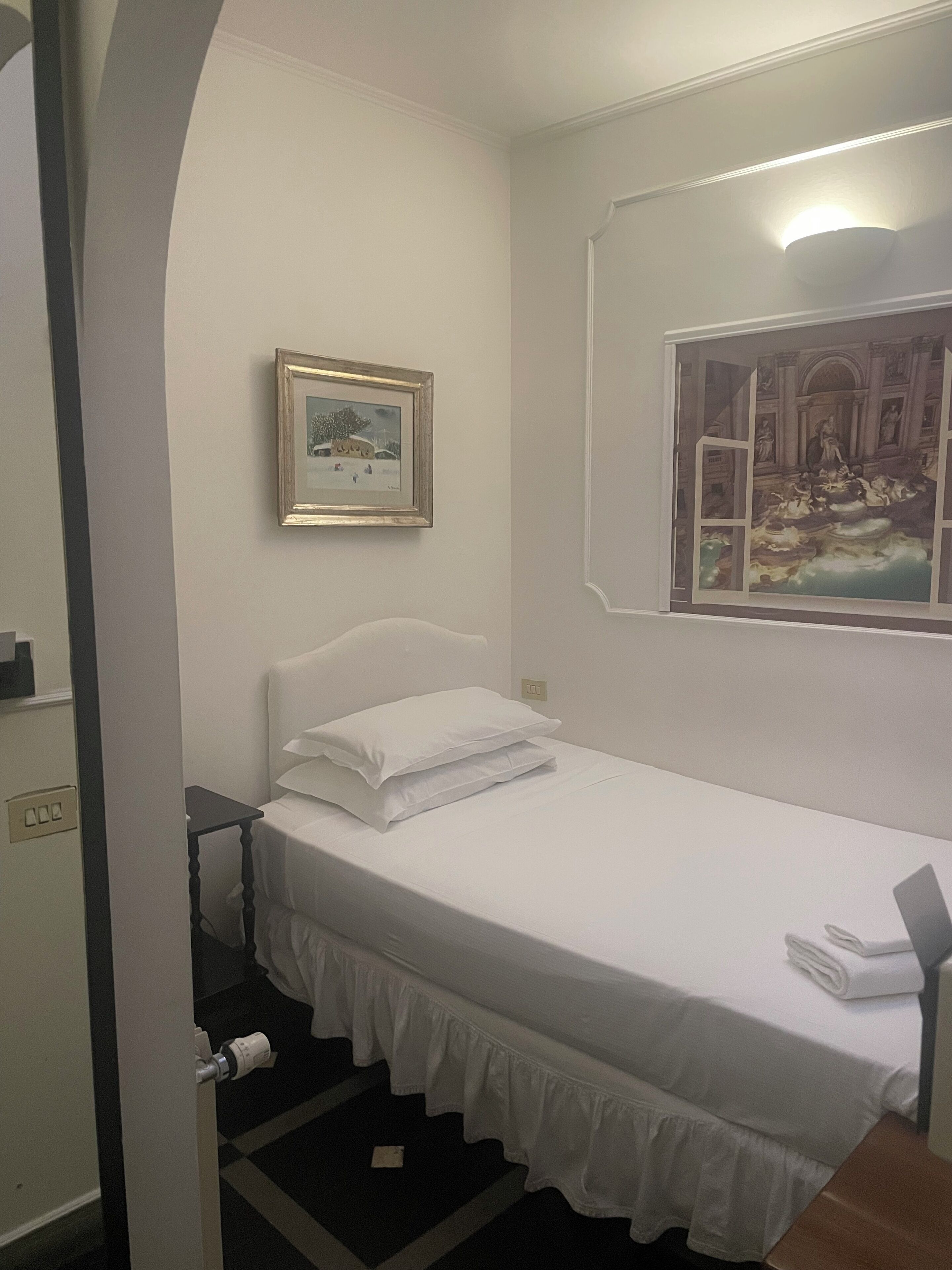A neatly made bed with white bedding, a framed picture on the wall, and a painting above the bed.