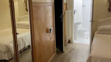 Habitación de hotel con armario de madera, espejo, cama, baño con ducha y una mesita.