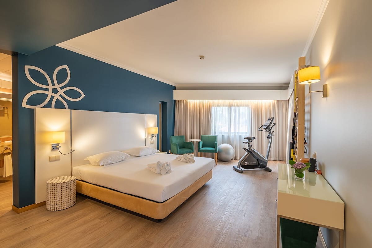 A modern hotel room with a large bed, a desk, a treadmill, and exercise balls.