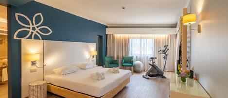 Una habitación de hotel moderna con una cama grande, un escritorio, una cinta de correr y pelotas de ejercicio.