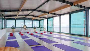 Ein geräumiges Zimmer mit großen Fenstern, Yogamatten und einer Holzbalkendecke.