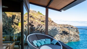 A modern balcony with a curved seating area, a glass railing, and a view of the ocean and rocky cliffs. - Sentido Galosol (Santa Cruz)