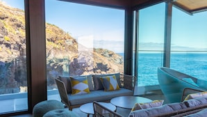 A modern interior with a sofa, chairs, and a table, overlooking a rocky coastline and the sea. - Sentido Galosol (Santa Cruz)
