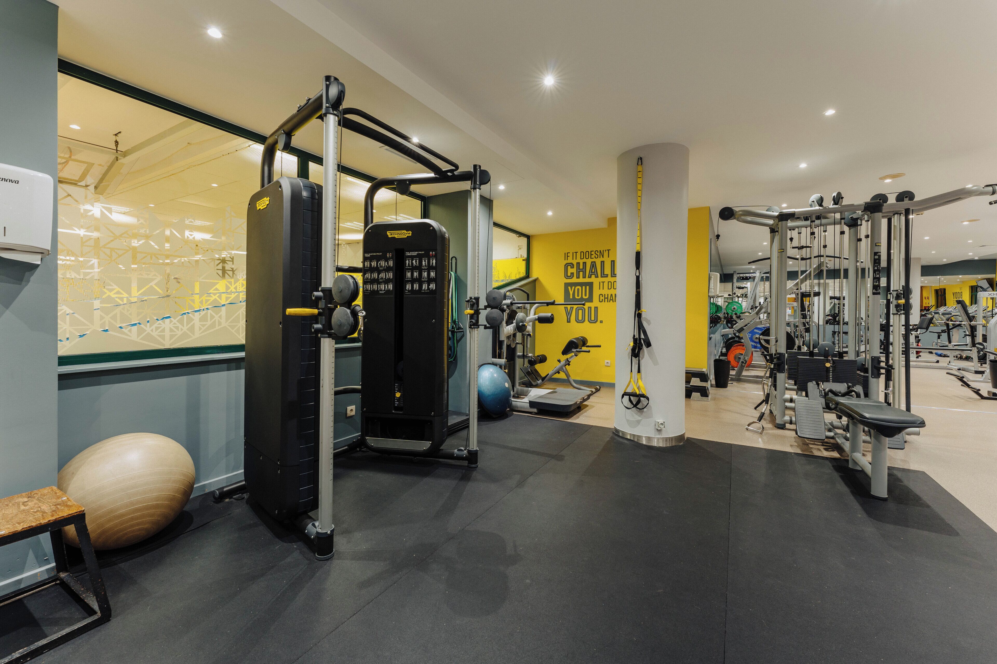 Ein Fitnessraum mit unterschiedlichen Trainingsgeräten, einem großen Übungsball und einem motivierenden Zitat an der Wand.