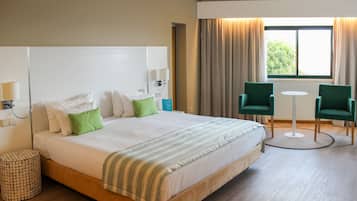 Une chambre d’hôtel avec un grand lit, deux chaises, une petite table et une fenêtre avec des rideaux.