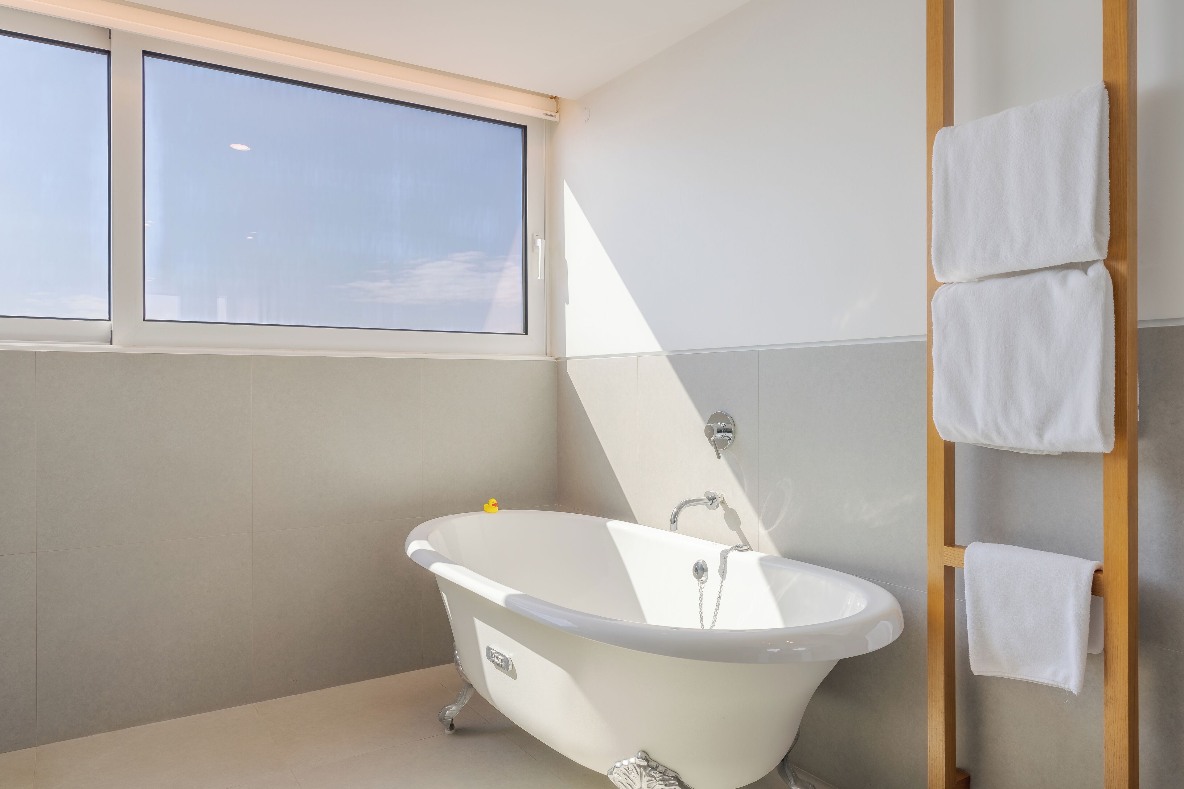 Un baño moderno con una bañera independiente, un ventanal y un perchero de madera.
