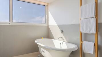 Un baño moderno con una bañera independiente, un ventanal y un perchero de madera.