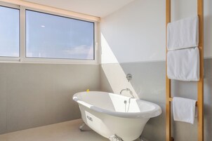 Un baño moderno con una bañera independiente, un ventanal y un perchero de madera.