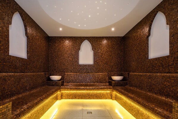 A spa room with mosaic-tiled walls, a central bench, and two side sinks.