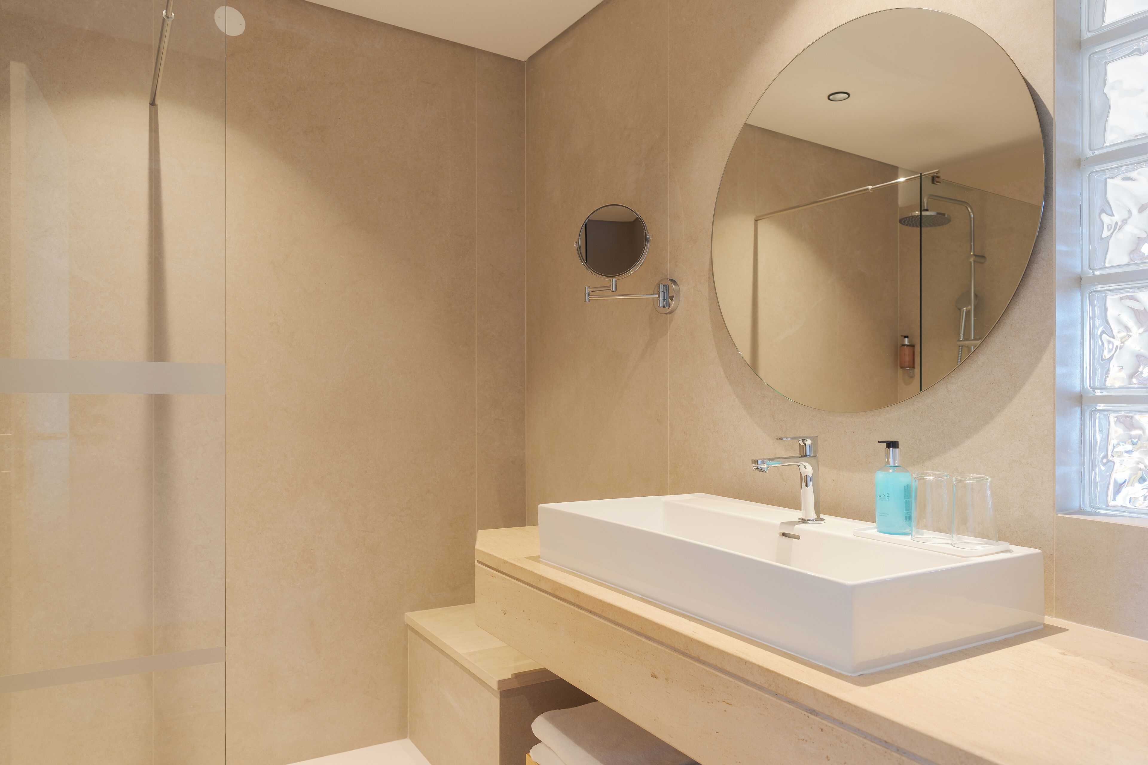 A modern bathroom with a large rectangular sink, a round mirror, and a glass-enclosed shower.