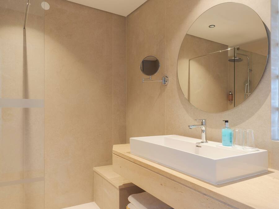 Une salle de bain moderne avec un grand lavabo rectangulaire, un miroir rond et une douche à parois de verre.