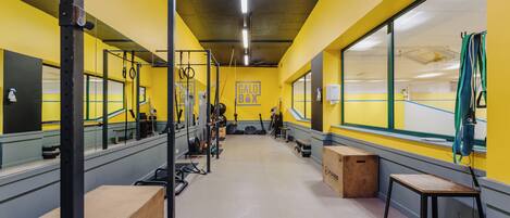 Un gimnasio con equipo de levantamiento de pesas, bancos y un ventanal grande.