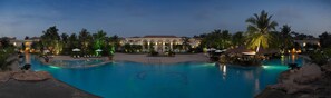A large outdoor swimming pool surrounded by palm trees and lounge chairs, with a building in the background. - The Zuri White Sands, Goa Resort & Casino (Varca)