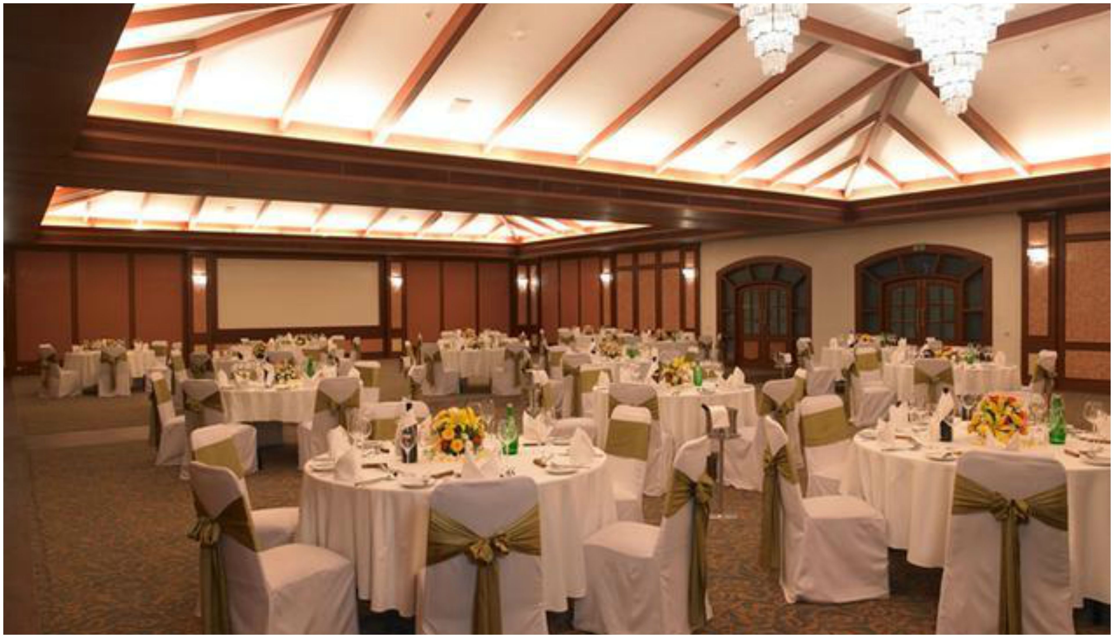 A large banquet hall with round tables, white tablecloths, and chairs with gold sashes.