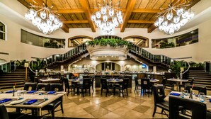 A spacious dining area with multiple tables and chairs, a central staircase, and a chandelier. - The Zuri White Sands, Goa Resort & Casino (Varca)