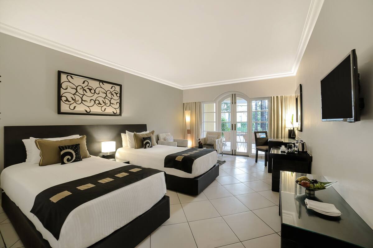 A hotel room with two beds, a desk, a TV, and a view of the outdoors.