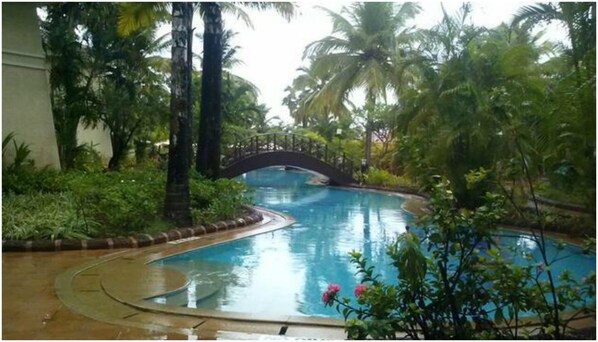 A swimming pool with a curved design, surrounded by lush greenery and palm trees. - The Zuri White Sands, Goa Resort & Casino (Varca)