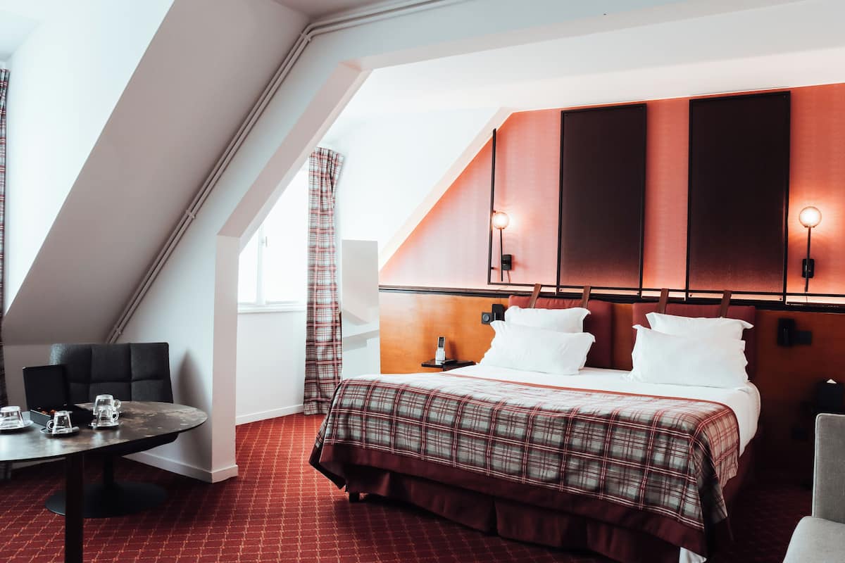 Ein Hotelzimmer mit einem Bett, einem Tisch mit Tassen, einem Stuhl und einem Fenster mit Vorhängen.