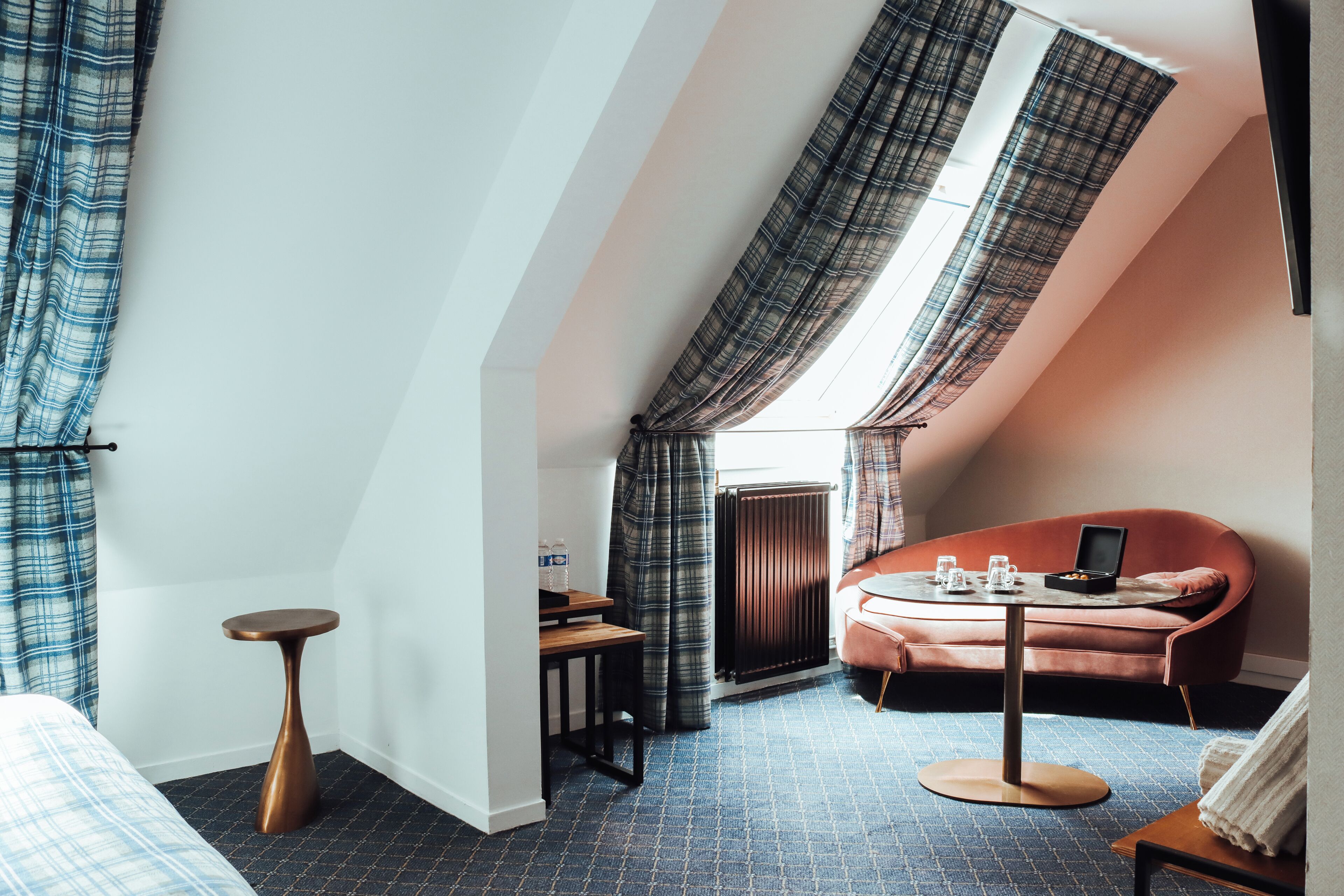A cozy room with a sloped ceiling, a small round table, a sofa, and a bed with a blue and white checkered duvet.