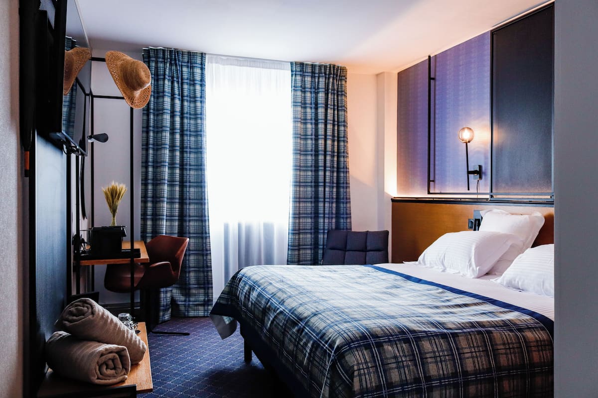 Ein Hotelzimmer mit Bett, Schreibtisch, Stuhl, Lampe und Vorhängen.