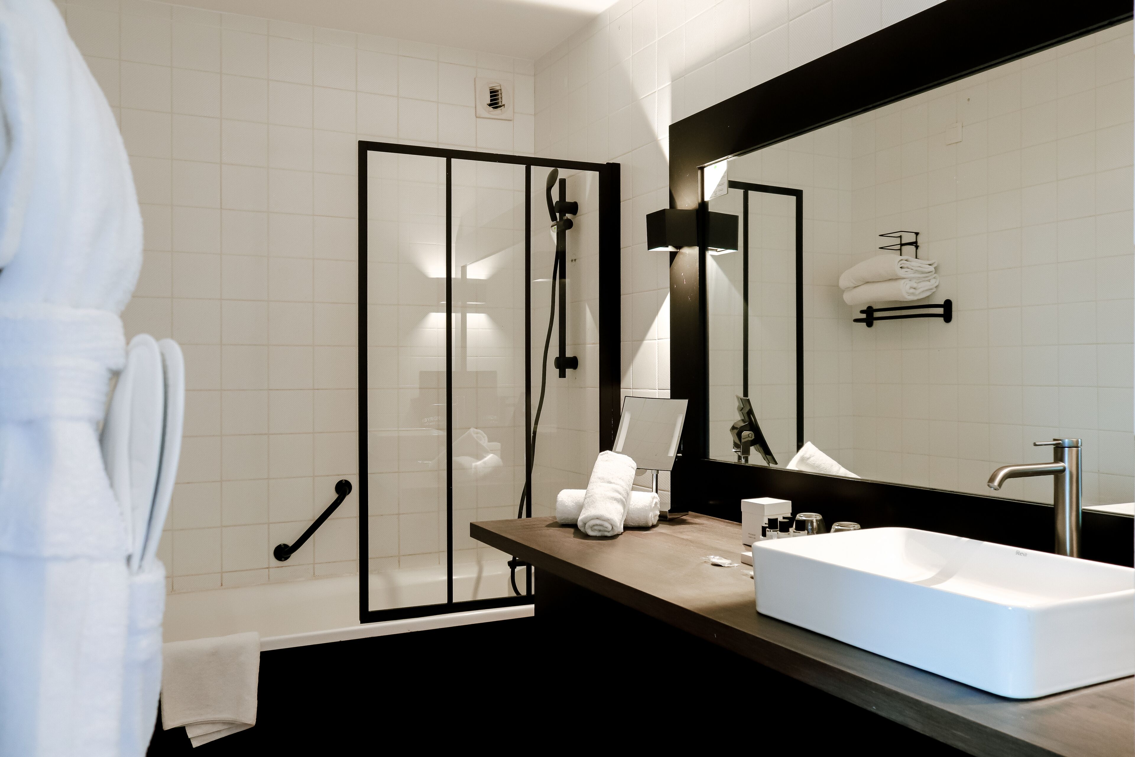 Un baño moderno con un lavamanos blanco, ducha con marco negro y un espejo grande.