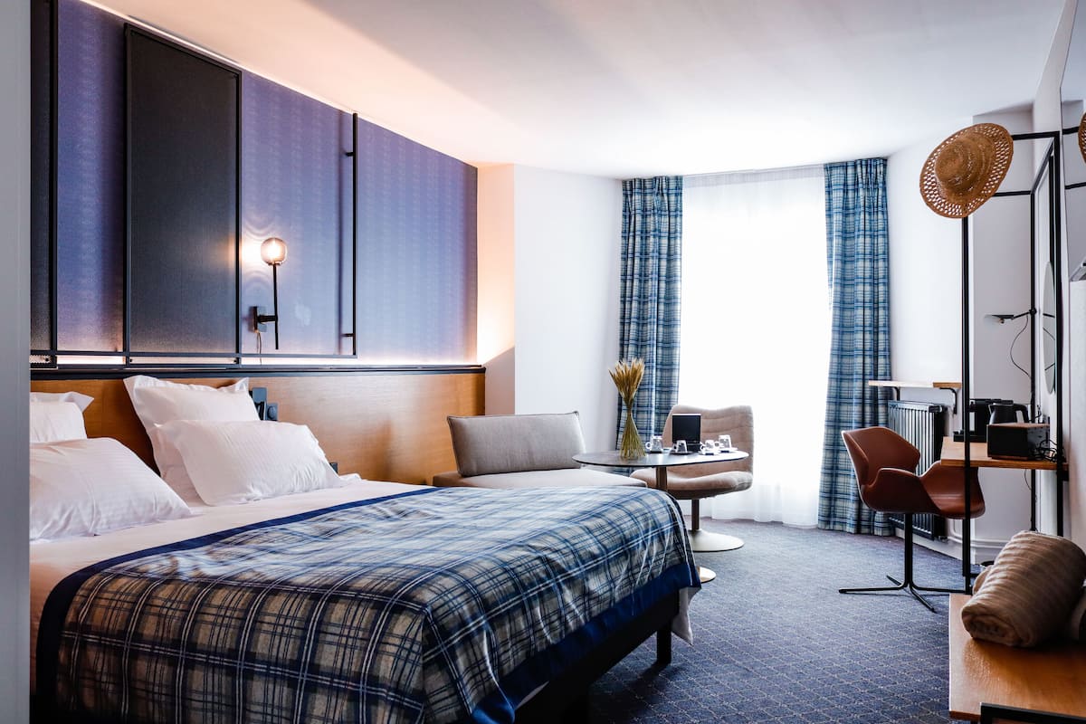 Ein Hotelzimmer mit einem großen Bett, einem Schreibtisch, einem Sessel und Blick ins Freie.