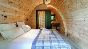 A cozy wooden cabin bedroom with a bed, pillows, a rolled towel, and a small desk with a chair.