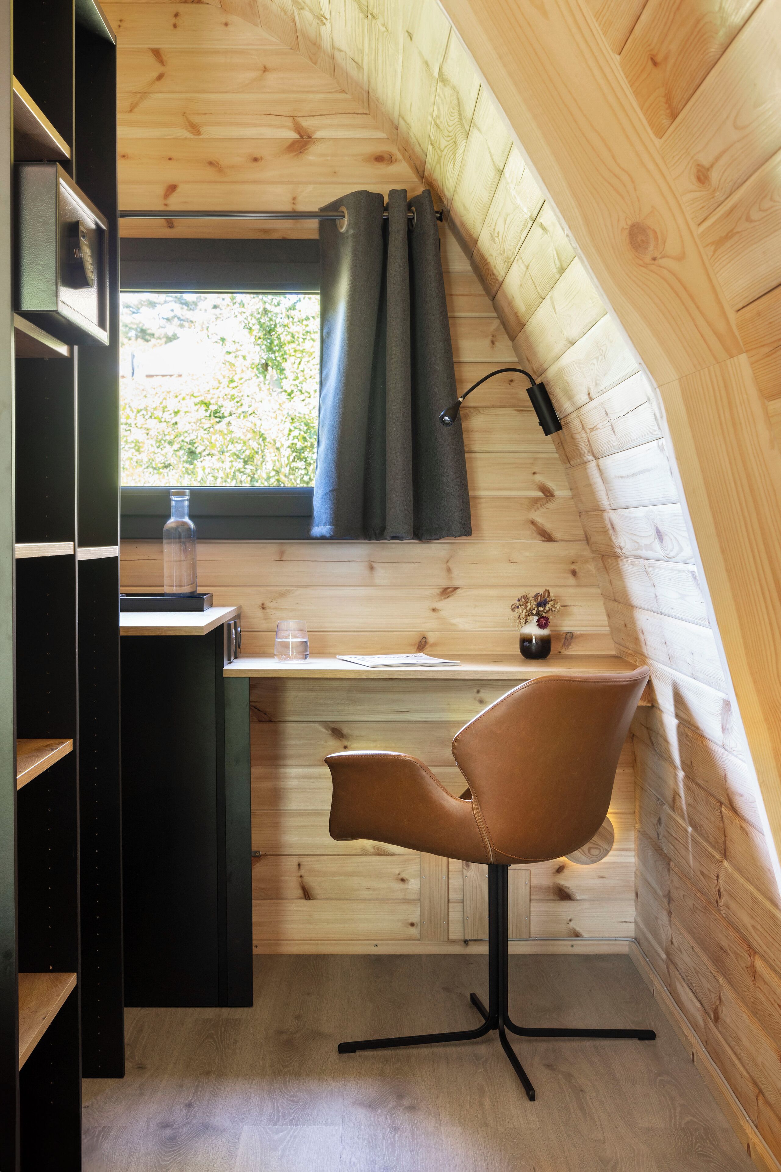 Una cocina compacta con paredes de madera, una ventana con cortinas, una mesita y una silla.