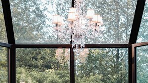 A room with a large window, a chandelier, and a table with a floral tablecloth.