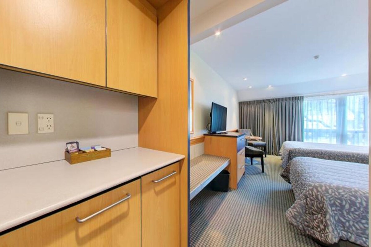 Una habitación de hotel con cama, escritorio, televisión y ventana con cortinas.