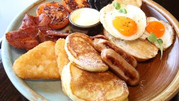 A plate of breakfast food including eggs, bacon, sausages, toast, and grilled tomatoes.