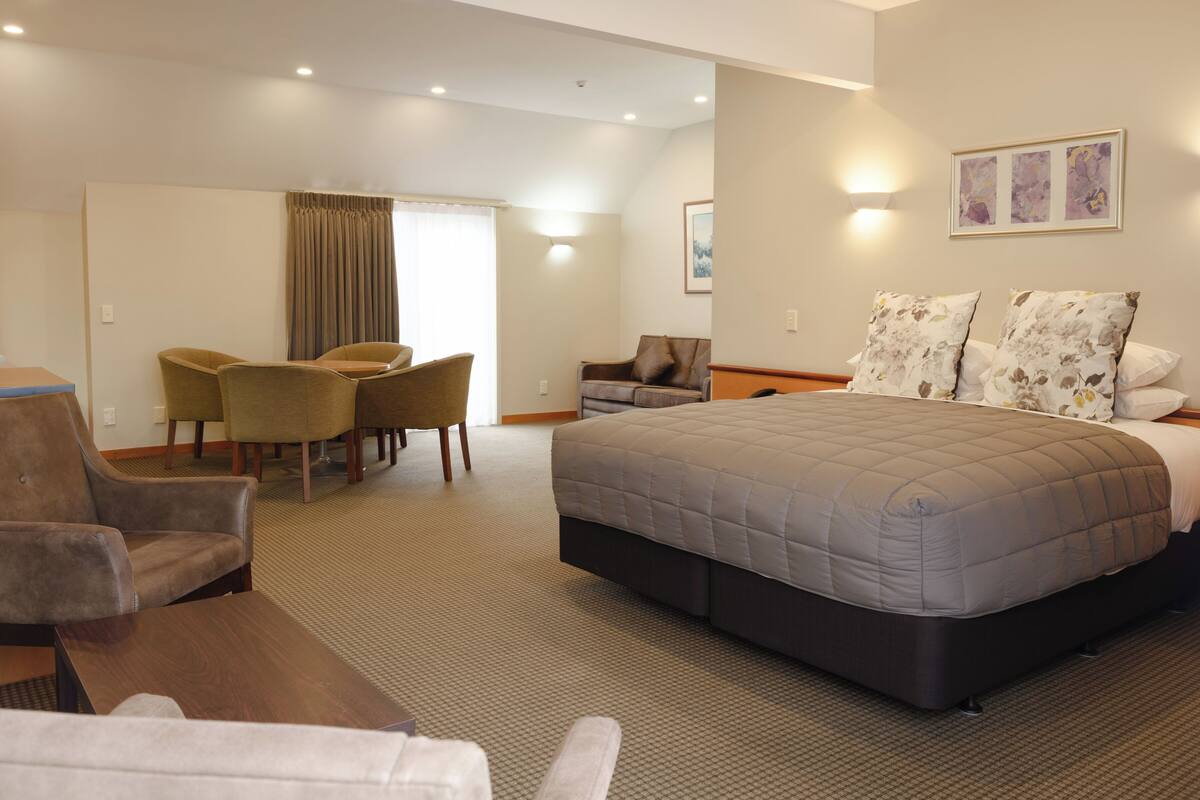 A hotel room with a large bed, a desk with chairs, a sofa, and a dining area.