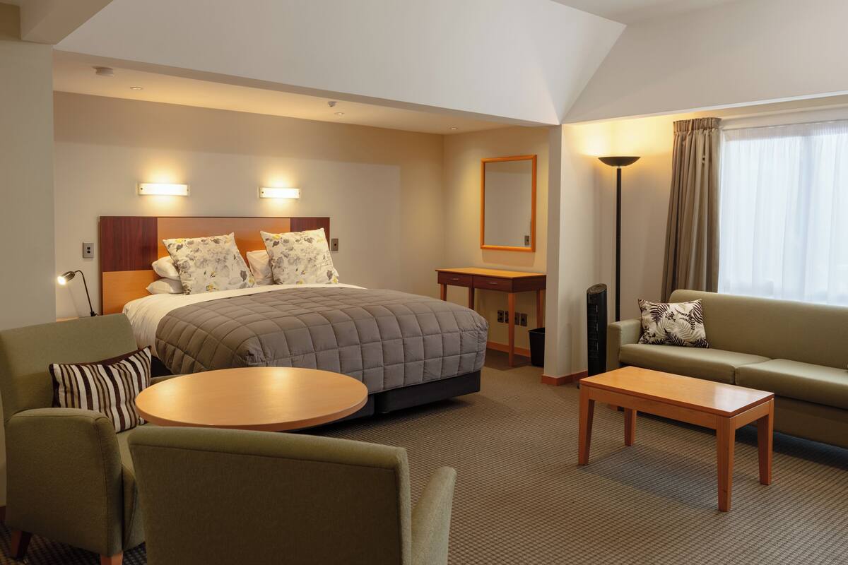 A hotel room with a bed, a sofa, a round table, a desk, and a lamp.