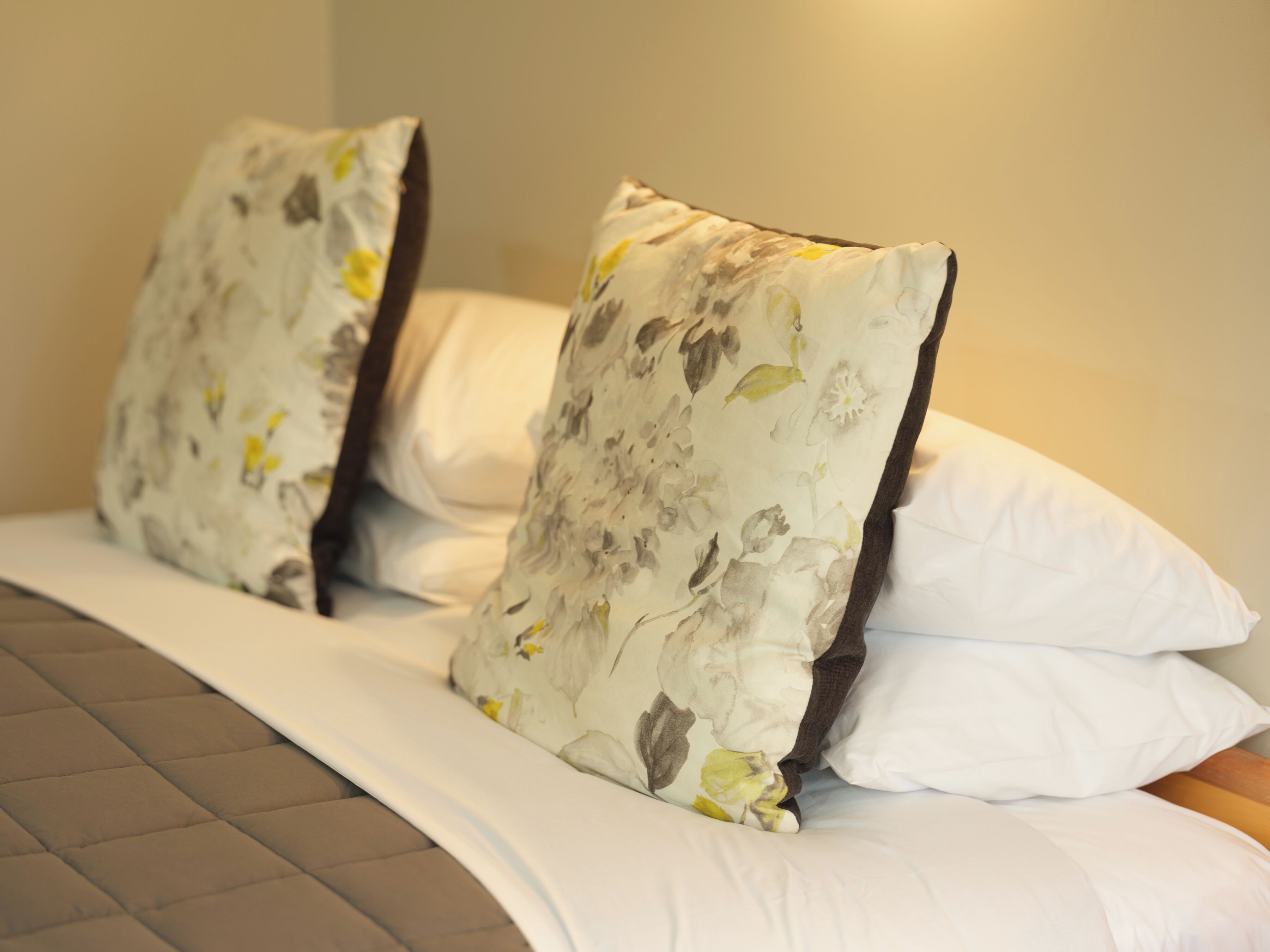 A bed with white bedding and floral-patterned pillows.
