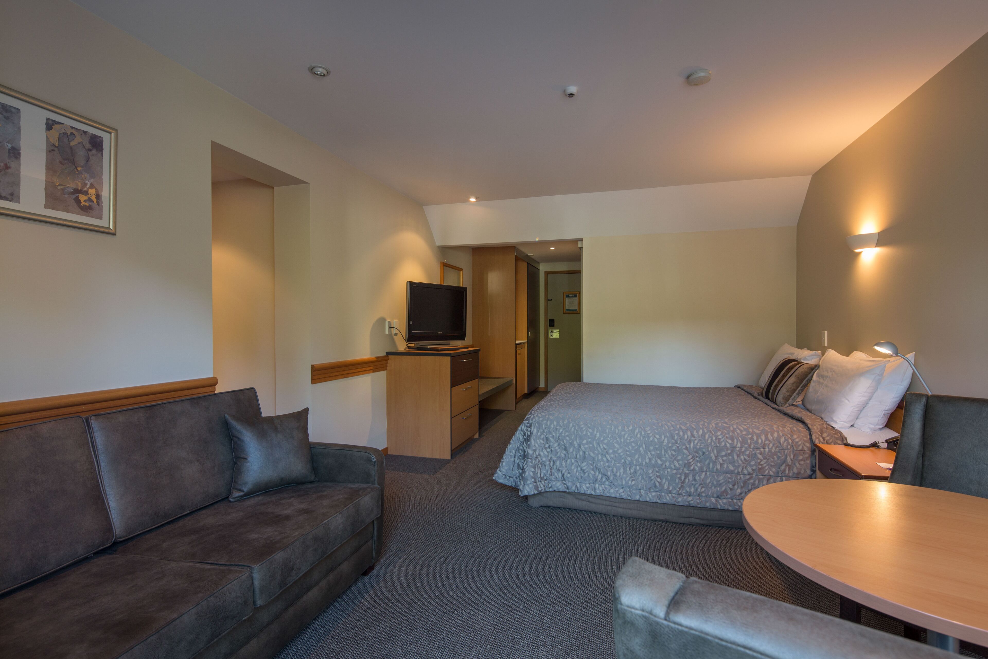 A hotel room with a bed, a sofa, a desk with a computer, and a TV.