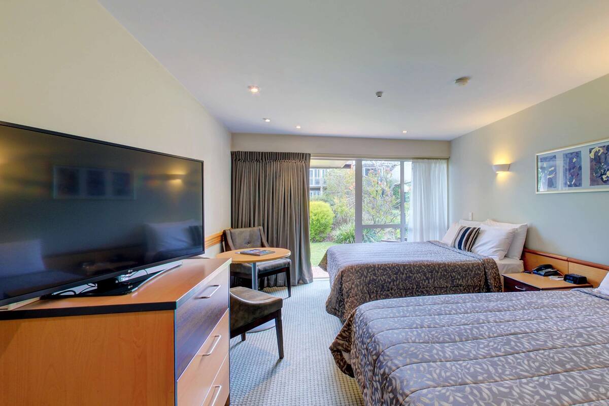 A hotel room with two beds, a TV, a desk, and a chair.