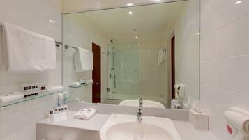 A modern bathroom with a large mirror, white sink, and glass shelves holding toiletries.